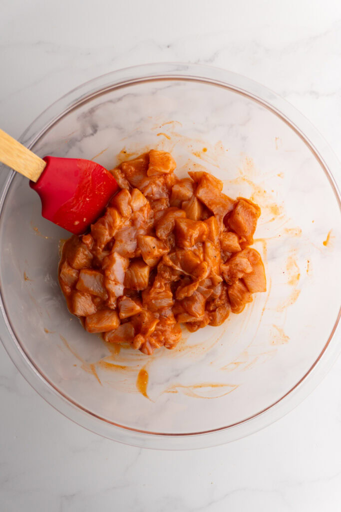 Diced raw chicken after being mixed with the buffalo sauce marinade.