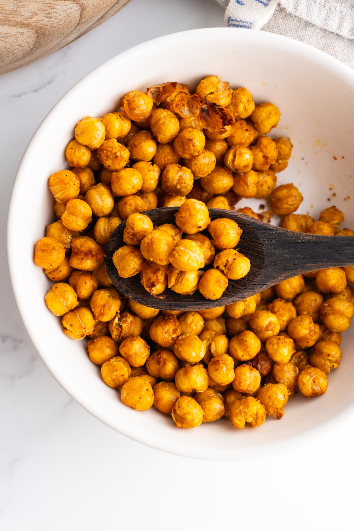 Spoon with some chickpeas on it with more crispy chickpeas on a bowl below it.