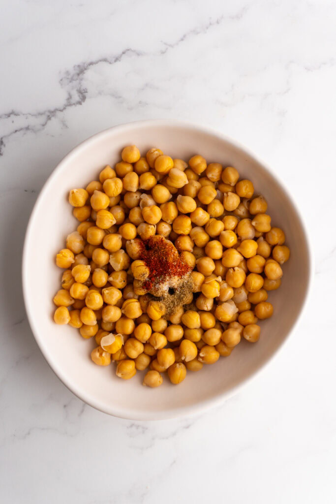 Chickpeas in a white bowl with olive oil and spices on top.