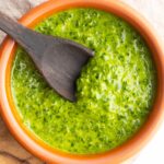 Close up of fresh basil pesto without nuts in a bowl with a wooden spoon.