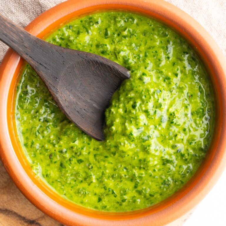 Close up of fresh basil pesto without nuts in a bowl with a wooden spoon.