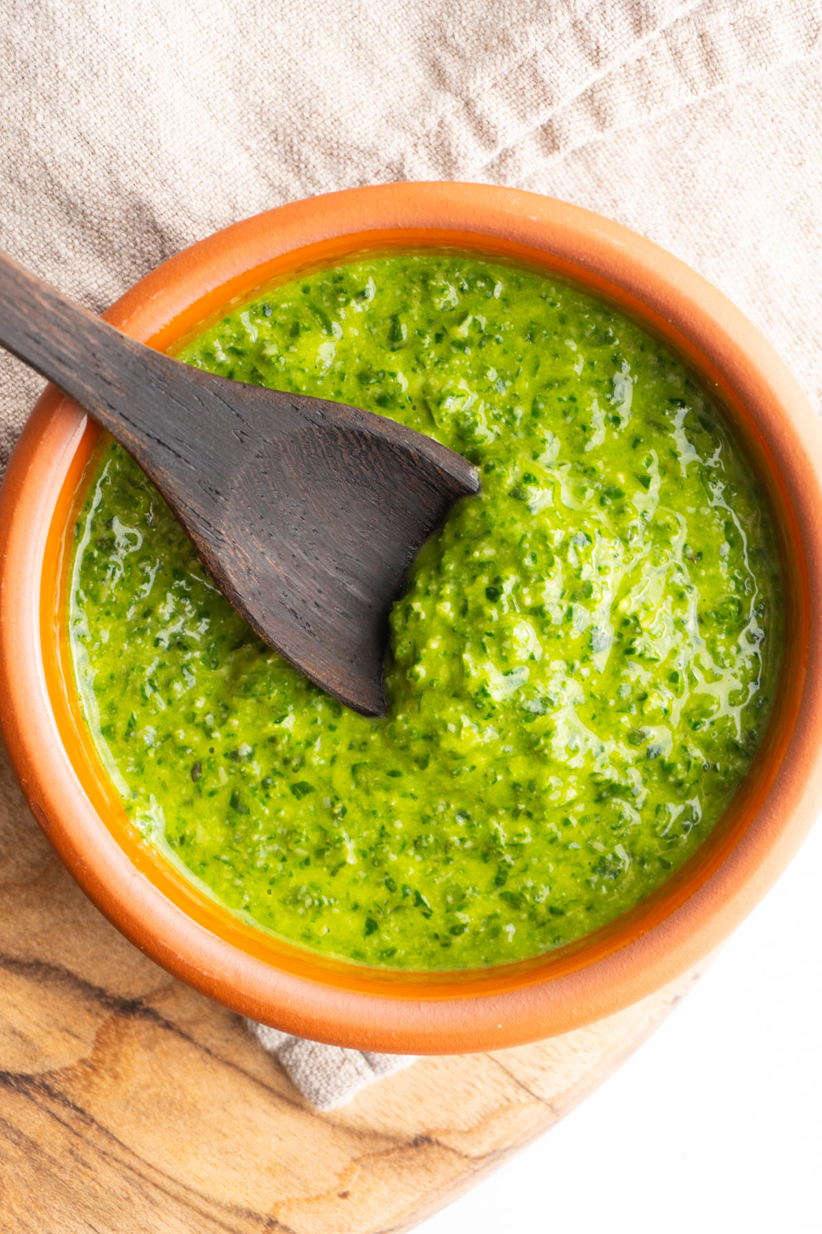 Overhead shot of fresh pesto sauce in a bowl with a wooden spoon.