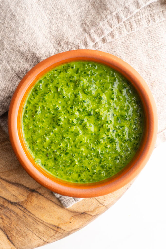 Fresh pesto sauce in a clay bowl on wooden background.