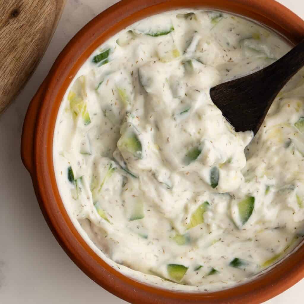 Tzatziki sauce in a clay bowl with a small wooden spoon.