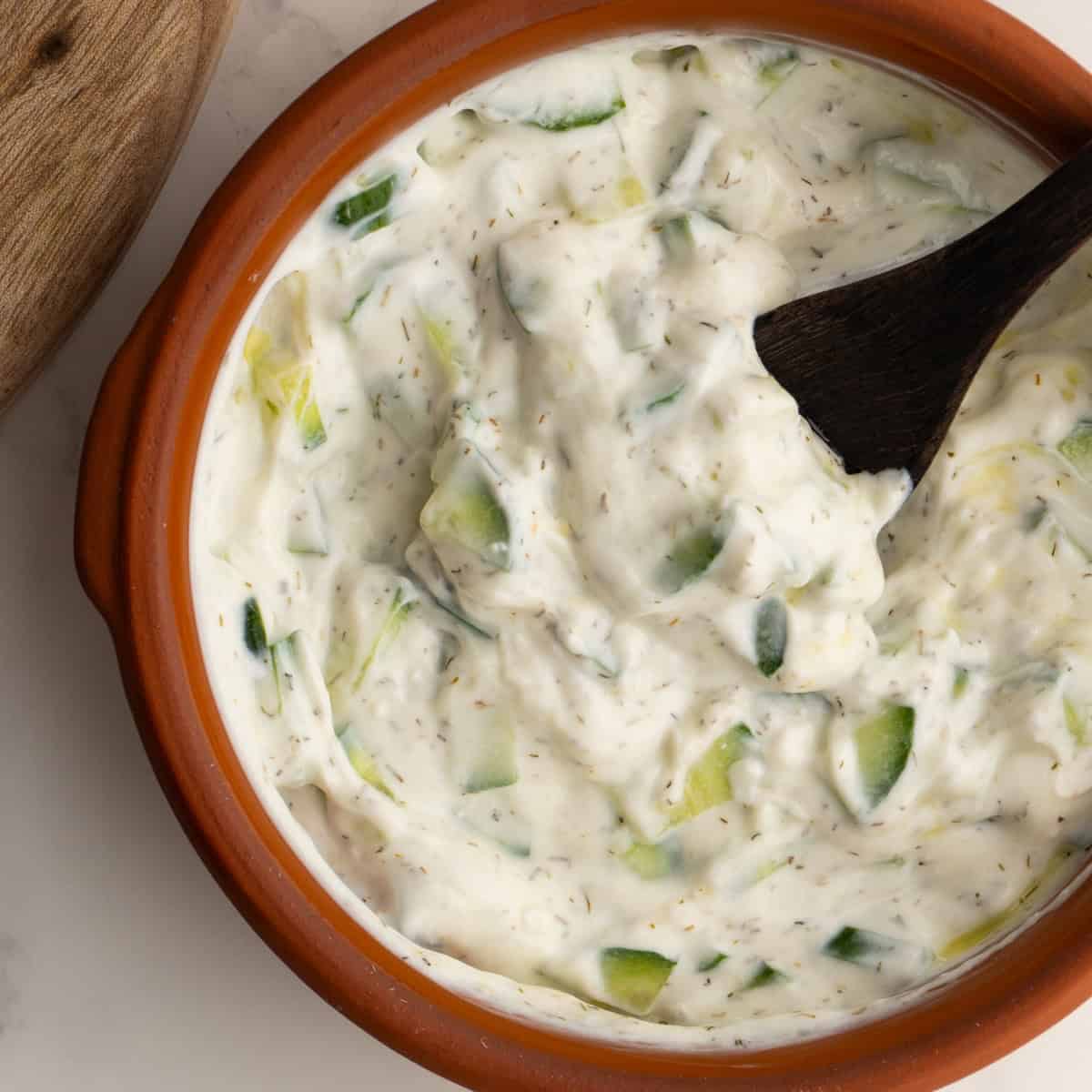 Tzatziki sauce in a clay bowl with a small wooden spoon.