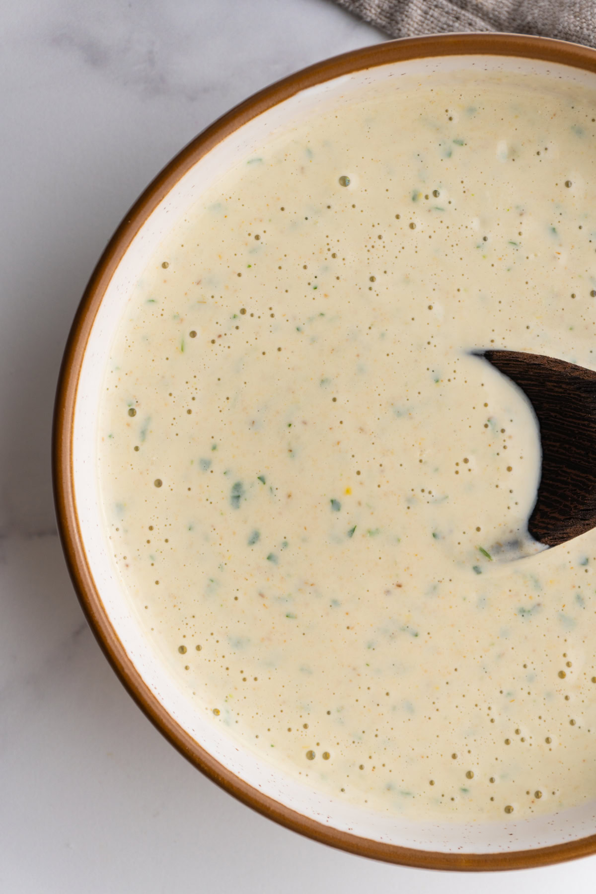 Close up of lemon tahini sauce in a bowl with a spoon.