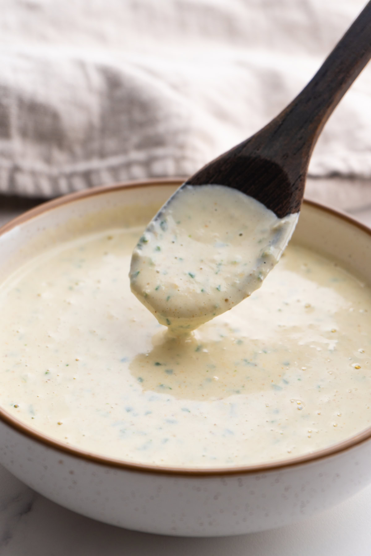 Spoon hovering over the lemon tahini sauce dripping some back into the bowl.