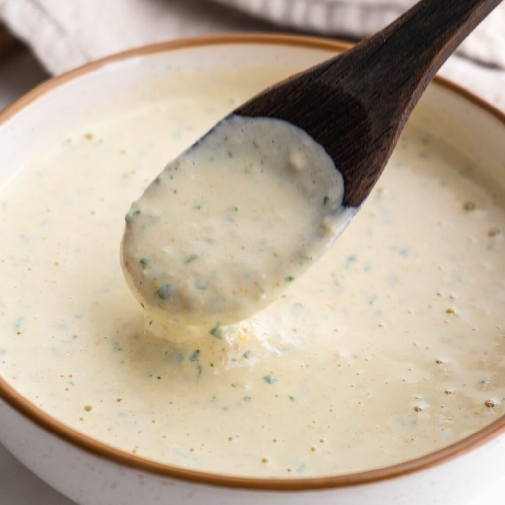 Lemon tahini sauce with a spoon dipped into it.