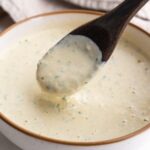 Lemon tahini sauce with a spoon dipped into it.