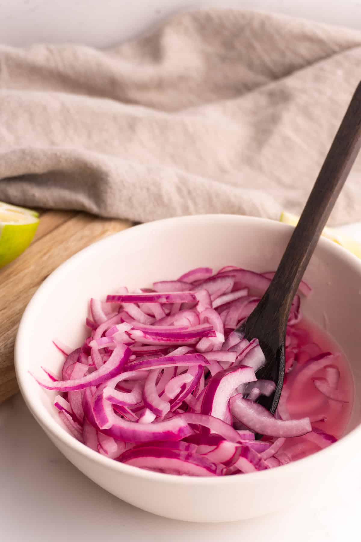 Side view of lime pickled onions in a white bowl with a small wooden spoon.