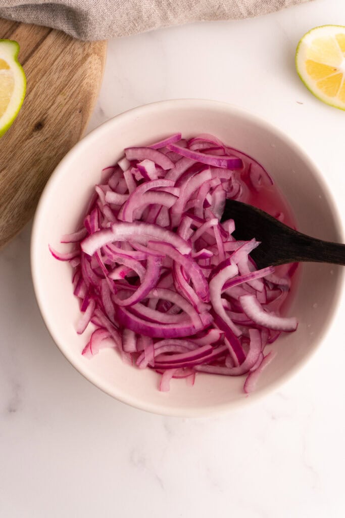 Overhead shot of lime pickled onions in a white bowl with a small wooden spoon.
