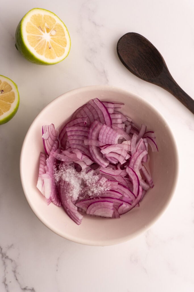 Sliced red onions in a bowl with lime juice and salt.