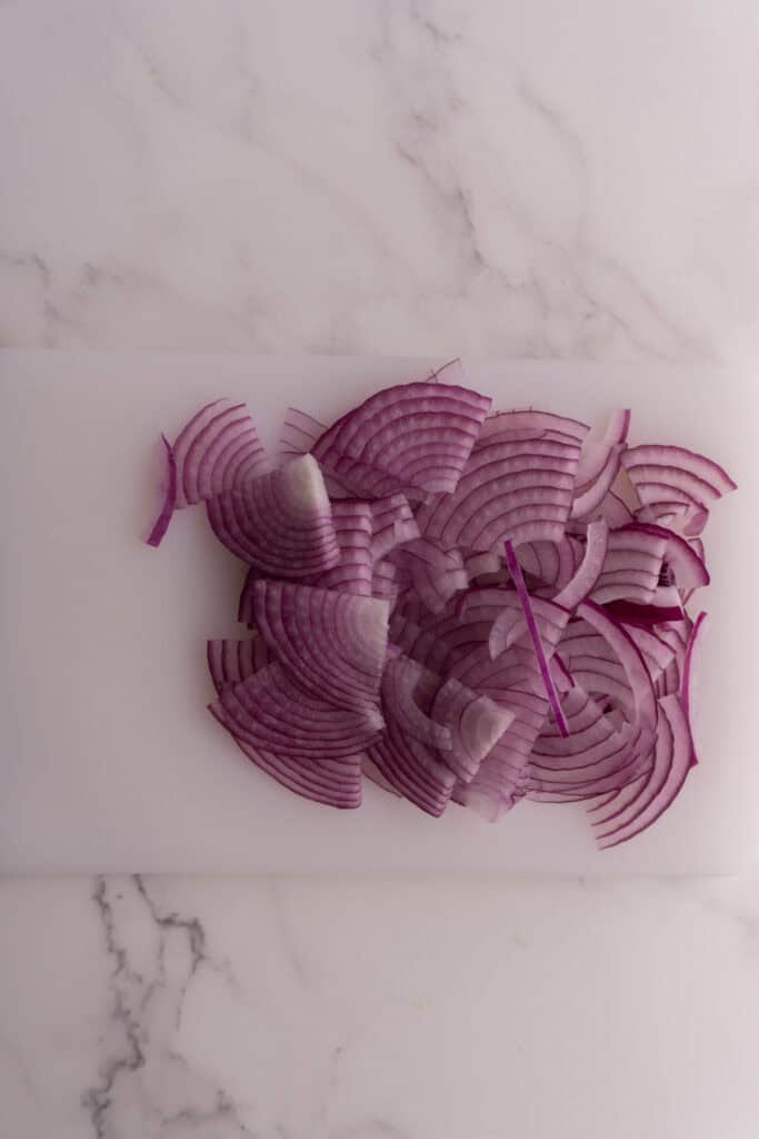 Sliced red onions on a white cutting board.