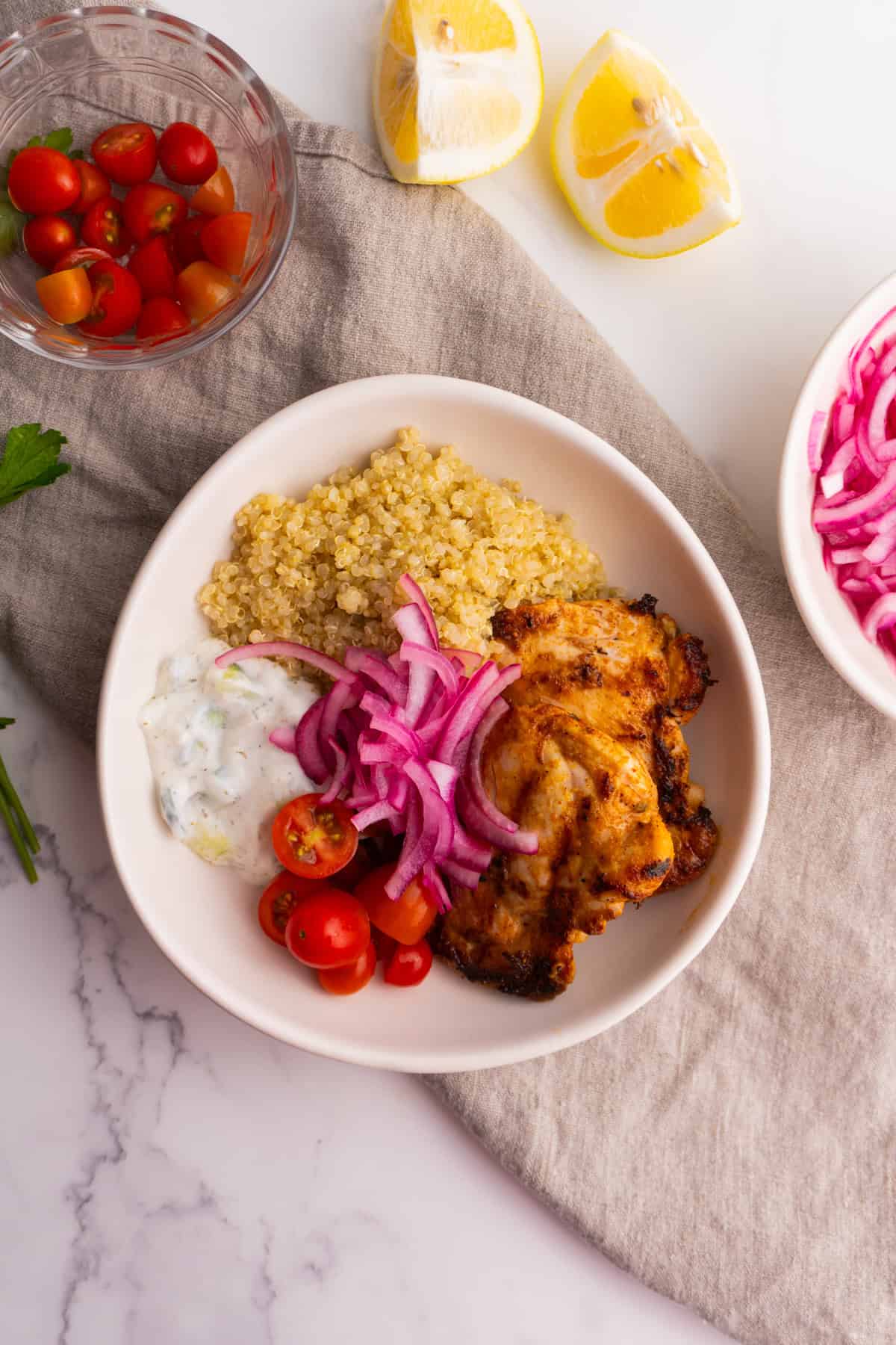 Mediterranean chicken quinoa bowl with tomatoes, lemons and onions on the side.