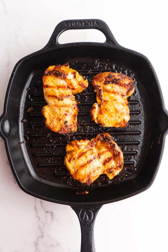 Chicken thighs cooking in a cast iron skillet griddle.