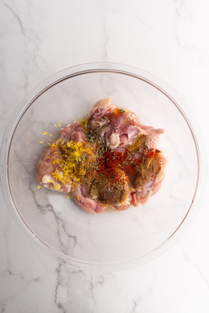 Chicken thighs in a mixing bowl with seasonings on top.