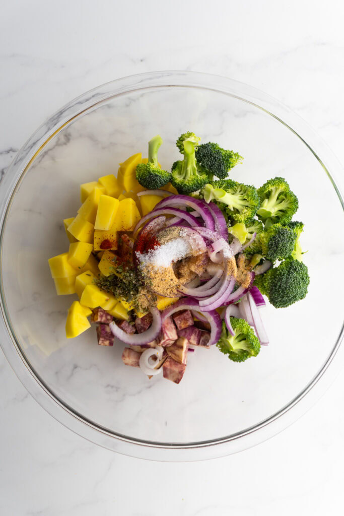 Diced vegetables in a mixing bowl with spices and olive oil.