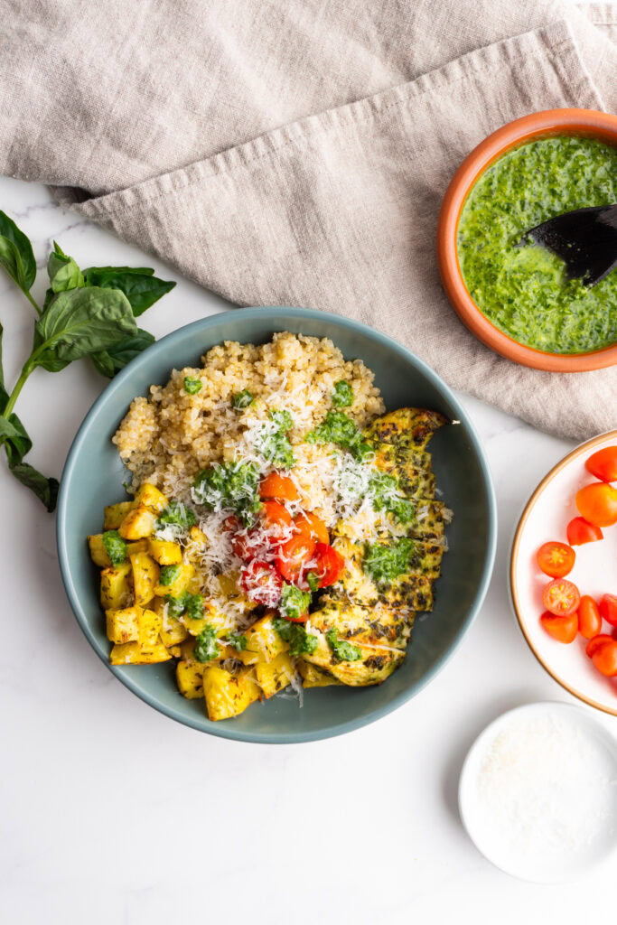 Pesto chicken bowl in a blue grey bowl next to more pesto sauce.