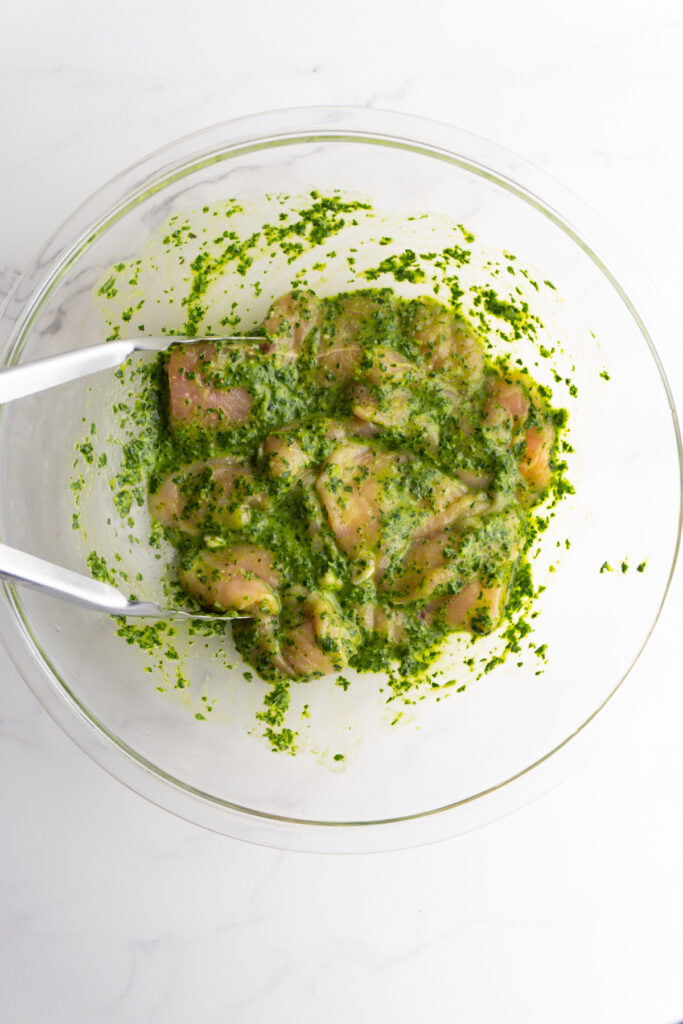 Chicken breasts mixed with pesto in a bowl.
