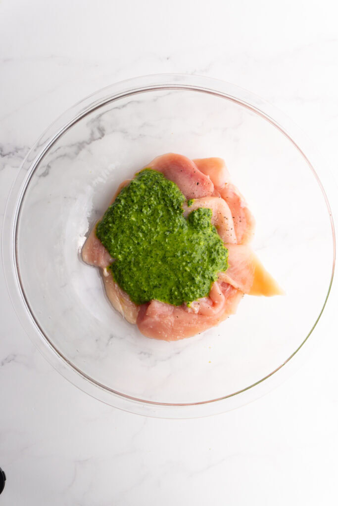 Pesto added to the chicken breasts in a bowl.