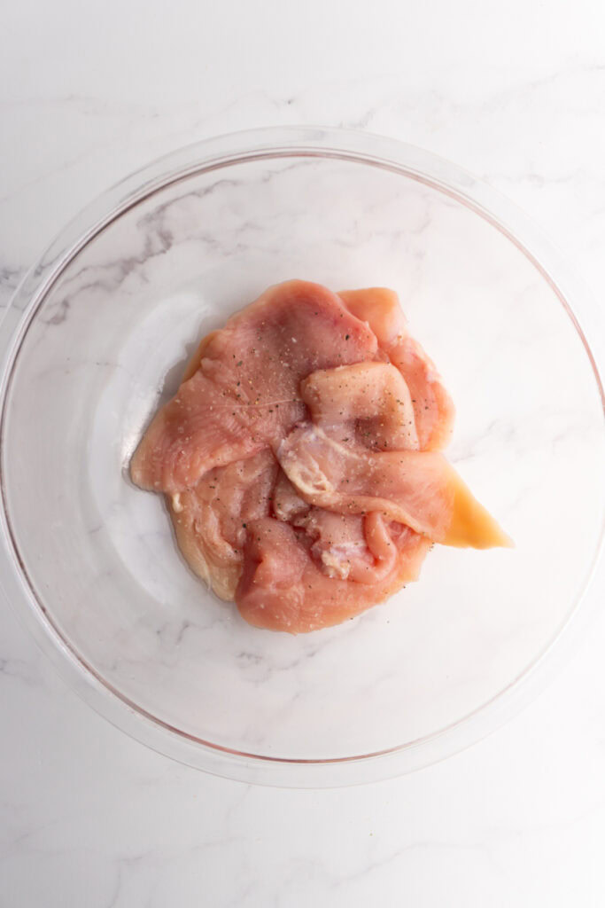 Chicken breasts in a bowl with salt and pepper ont op.
