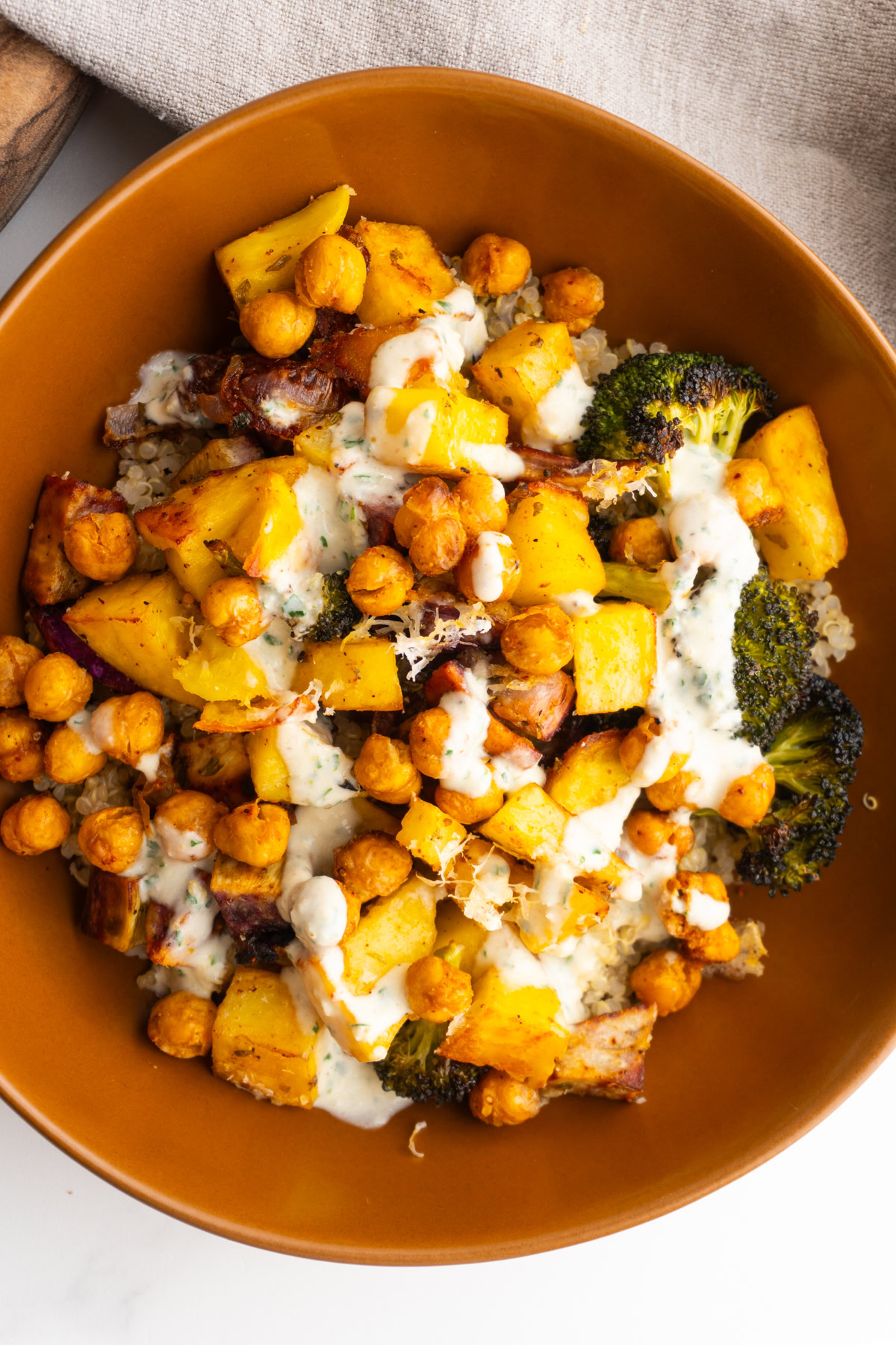 Quinoa in a bowl with roasted vegetables, chickpeas, and lemon tahini sauce on top.