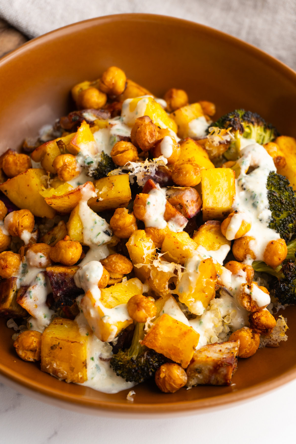 Roasted vegetables with quinoa, chickpeas and a sauce on top in a bowl.