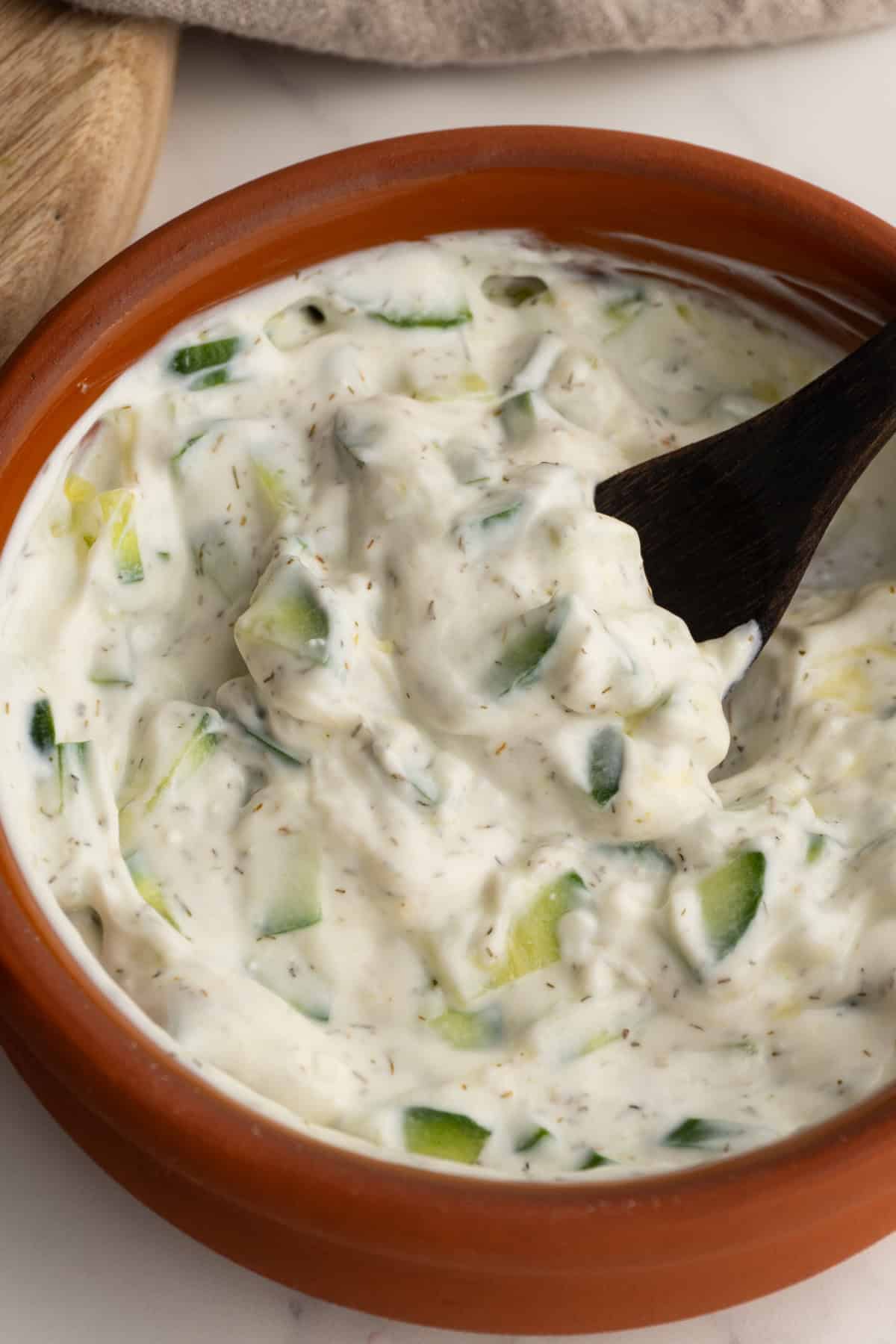 Close up of homemade tzatziki sauce in a clay bowl with a small spoon.