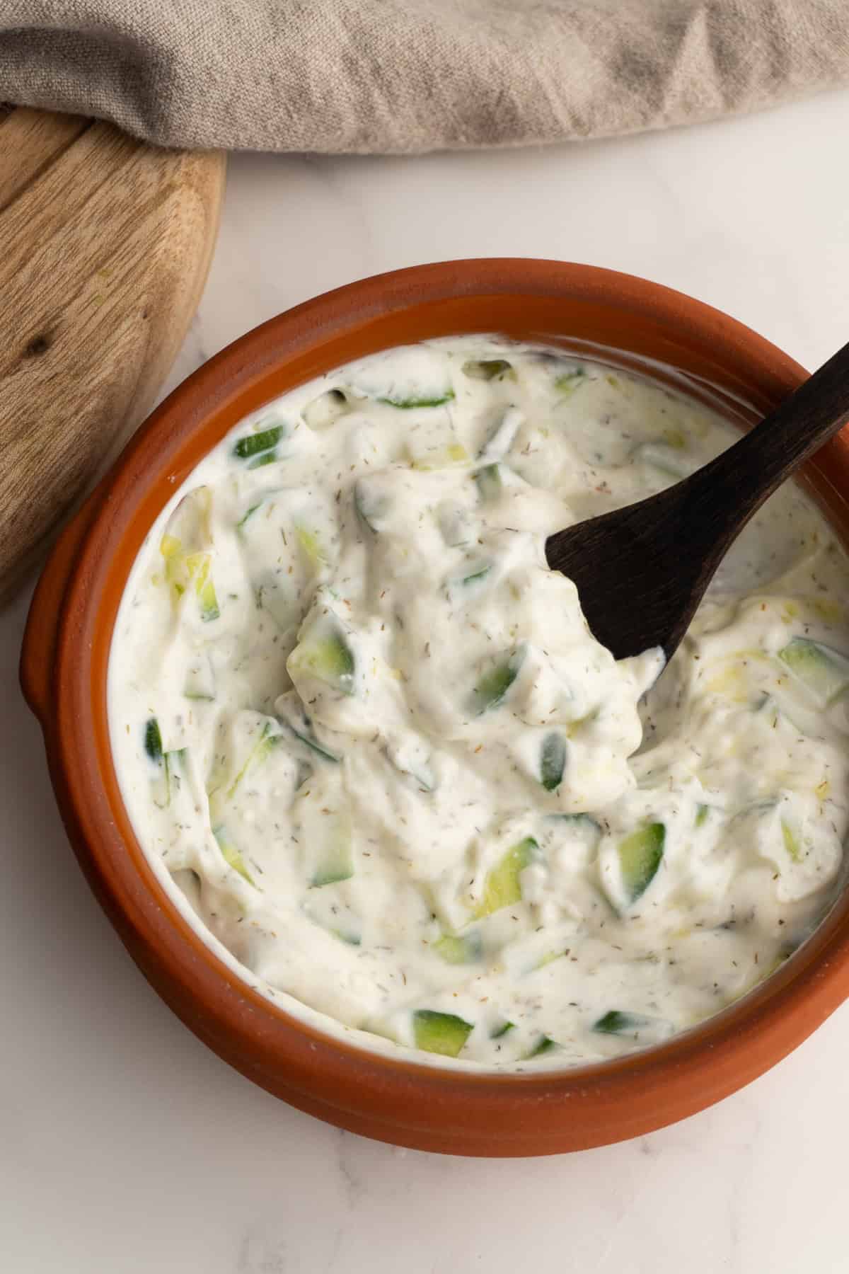 Tzatziki sauce in a clay bowl with cucumber chunks.