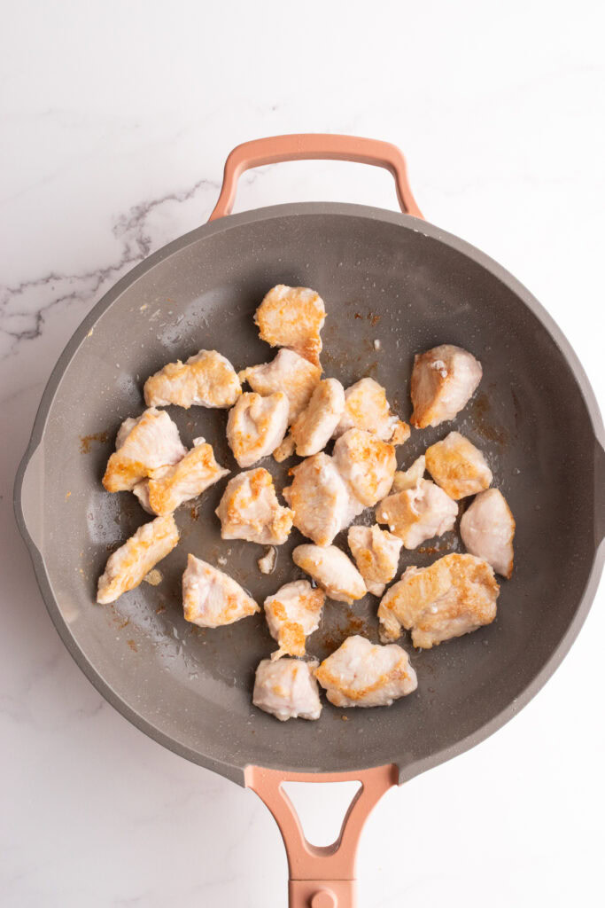 Chicken pieces in a skillet on a white background.