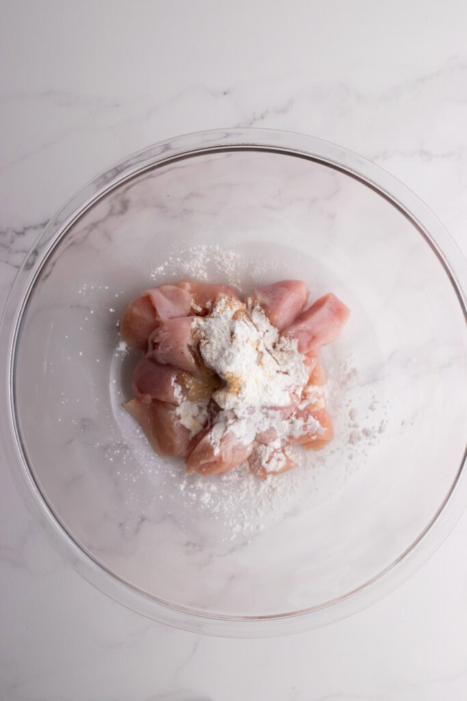 A bowl of chicken in a clear bowl with cornstarch and garlic powder.