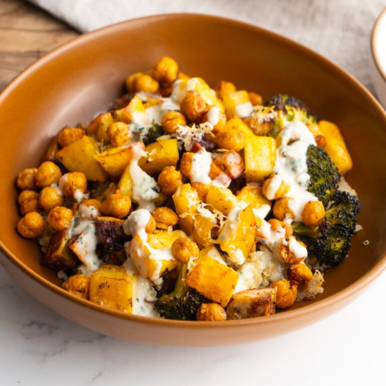 Side view of a roasted veggie bowl with lemon tahini sauce on top.
