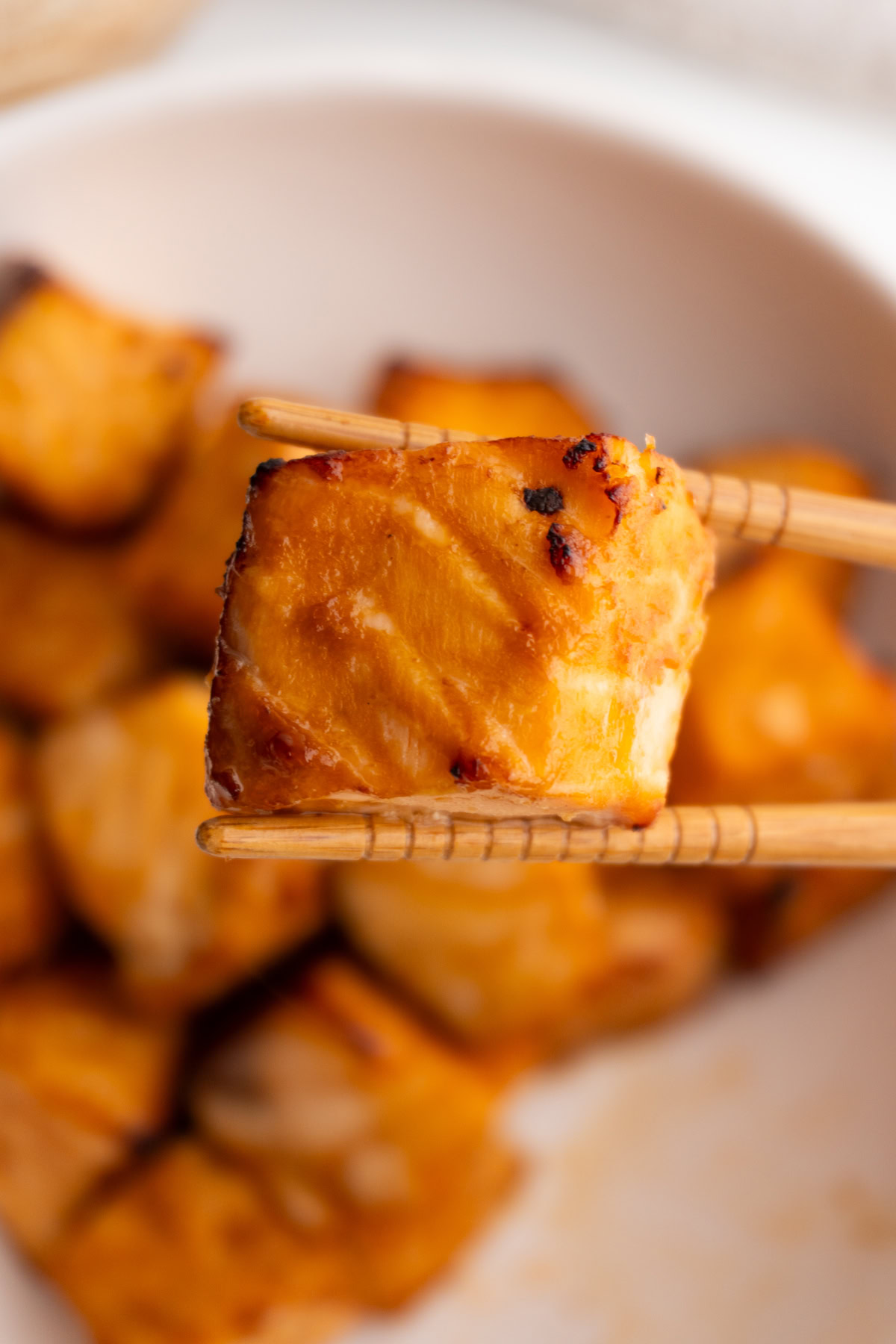 Chopsticks holding up a salmon bite with more in below it.