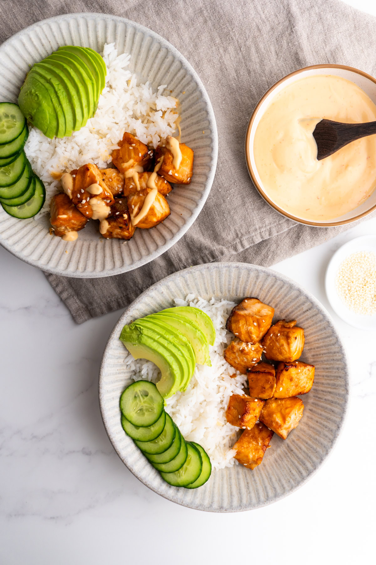 Two air fryer salmon bowls next to a small bowl of spicy mayo.