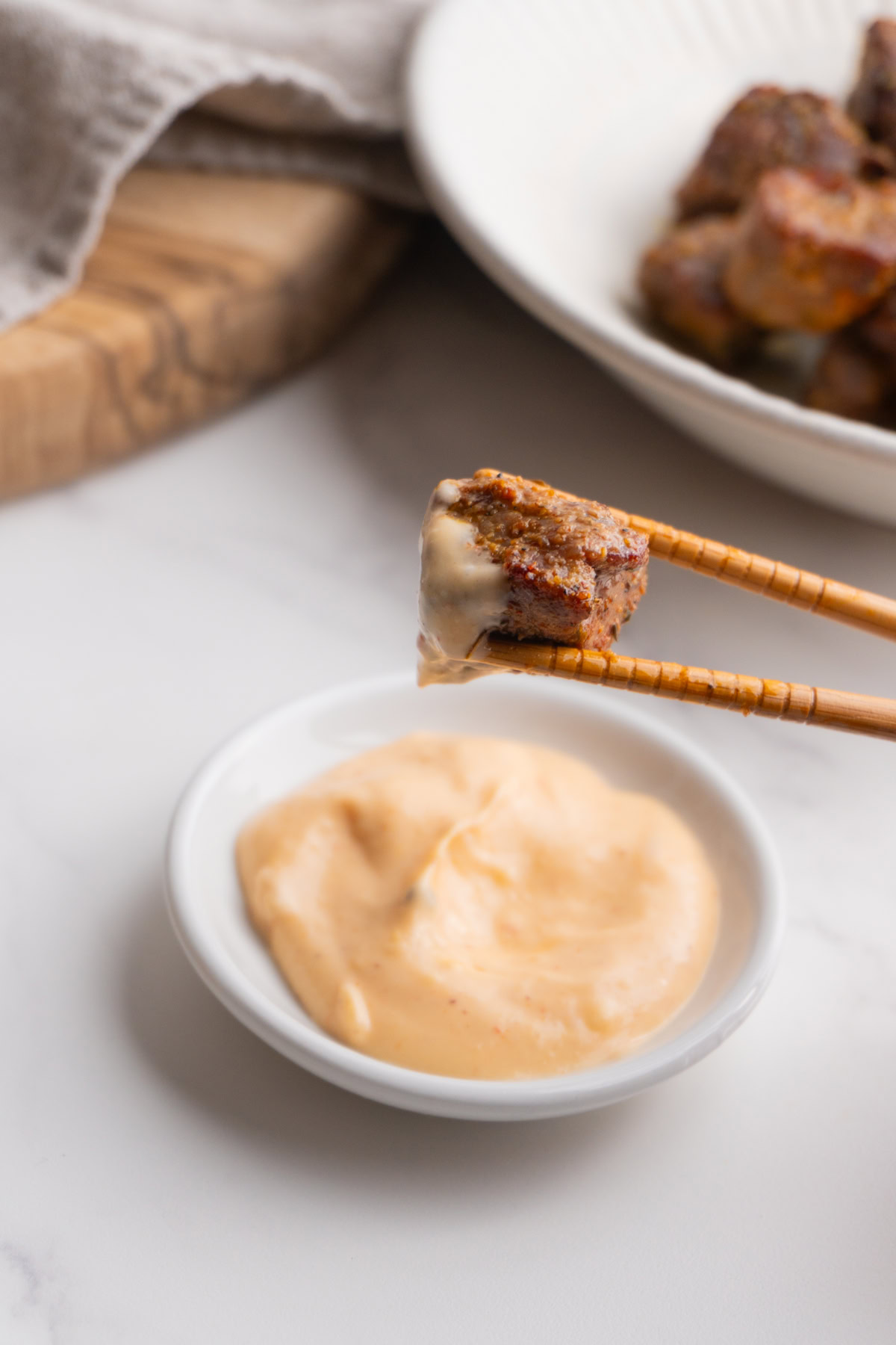 Chopsticks holding a steak bite that was dipped in yum yum sauce.