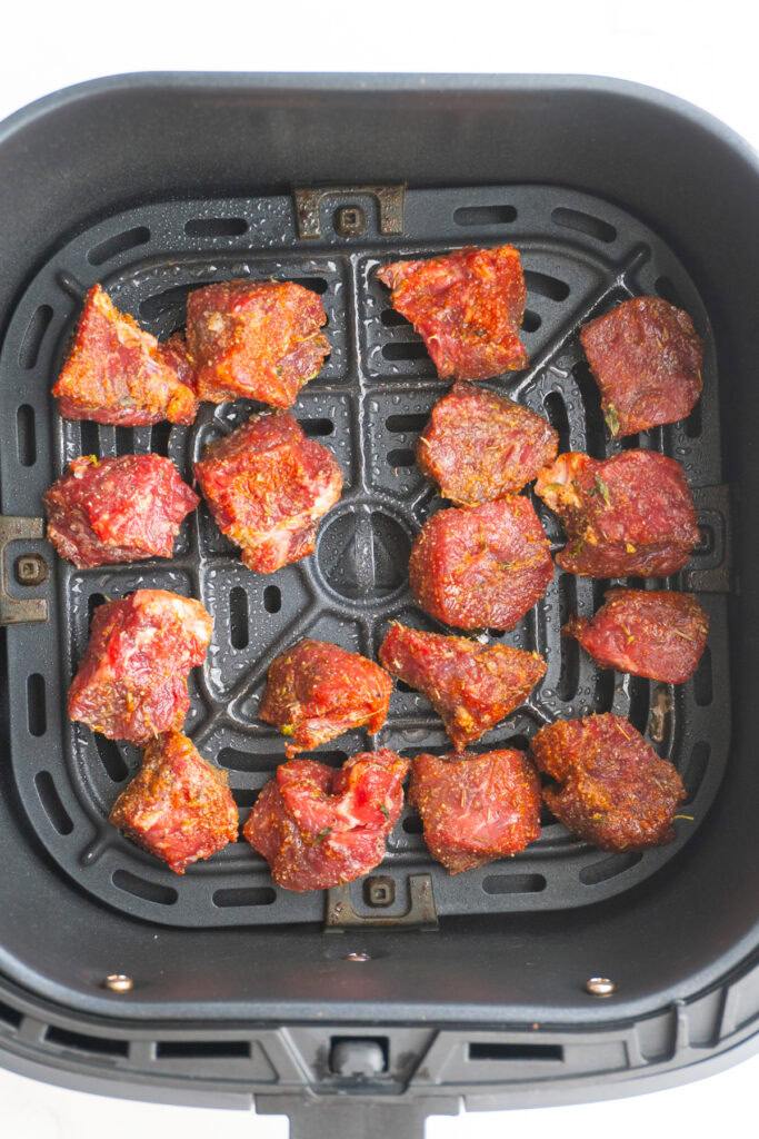 Seasoned steak added to the air fryer basket to cook.
