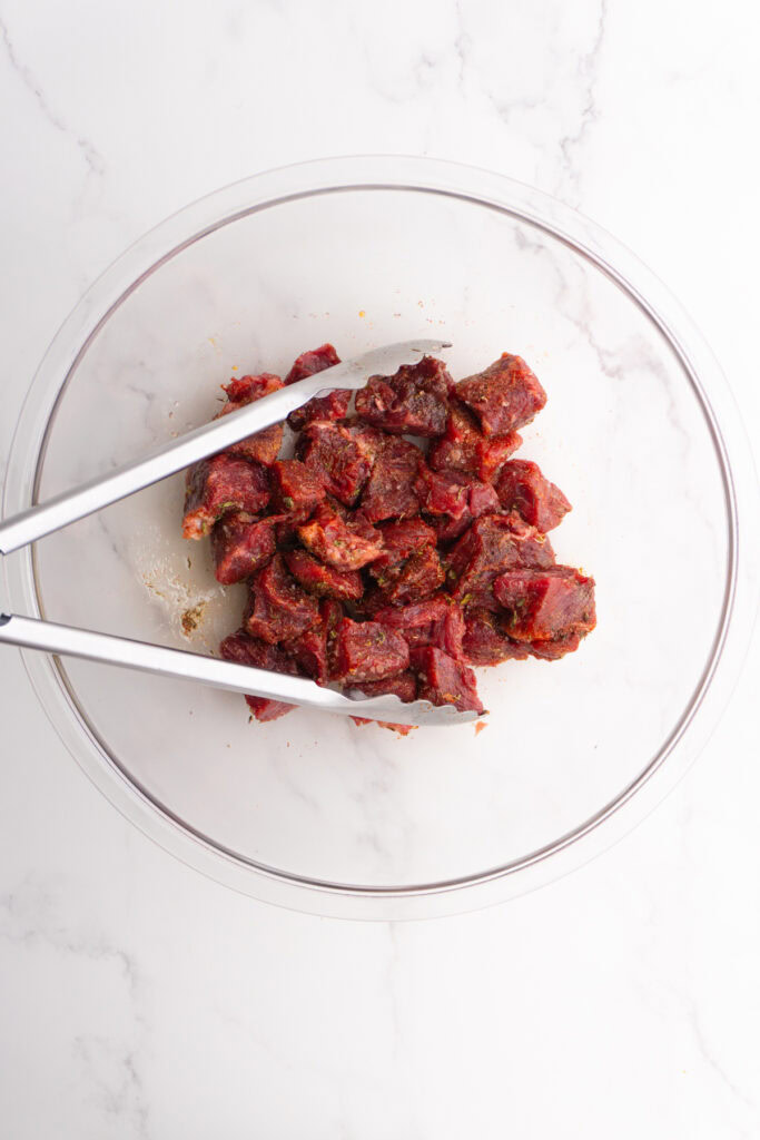 Steak bites mixed with seasoning in a bowl.