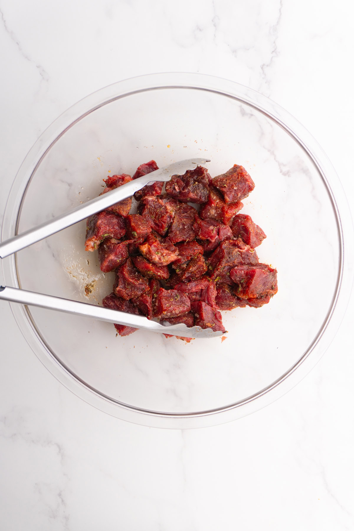Steak bites mixed with seasoning in a bowl.