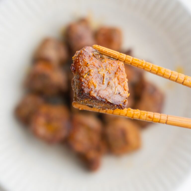 Chopsticks holding a steak bite hovering over more steak bites.