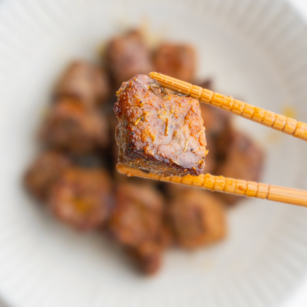 Chopsticks holding a steak bite hovering over more steak bites.