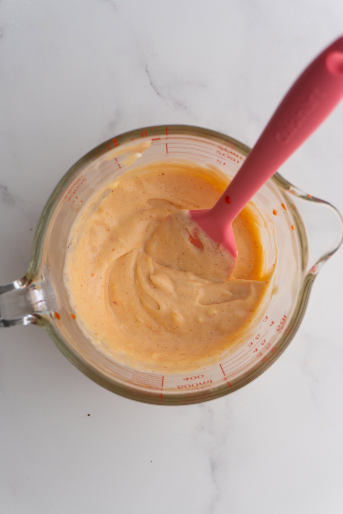 Yum yum sauce in a glass measuring cup with a small rubber spatula.
