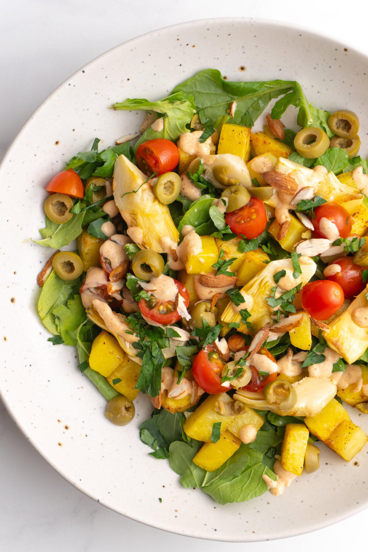 Closer shot of patatas bravas salad bowl, with arugula, potatoes, artichokes, and tomatoes.