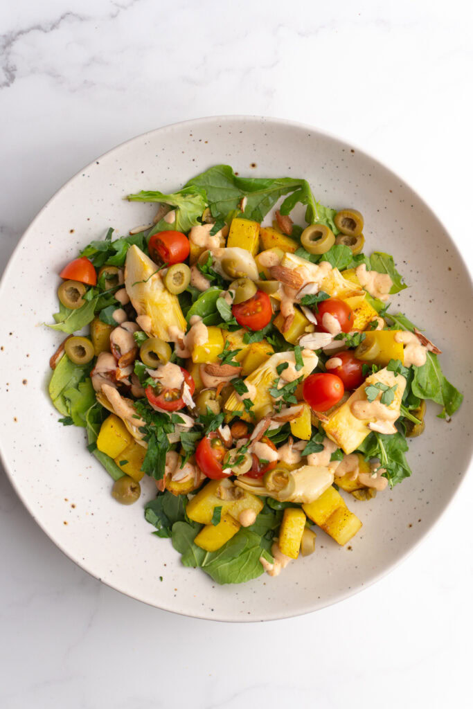 Patatas bravas salad bowl in a white speckled bowl with lots of veggies on a bed of arugula.