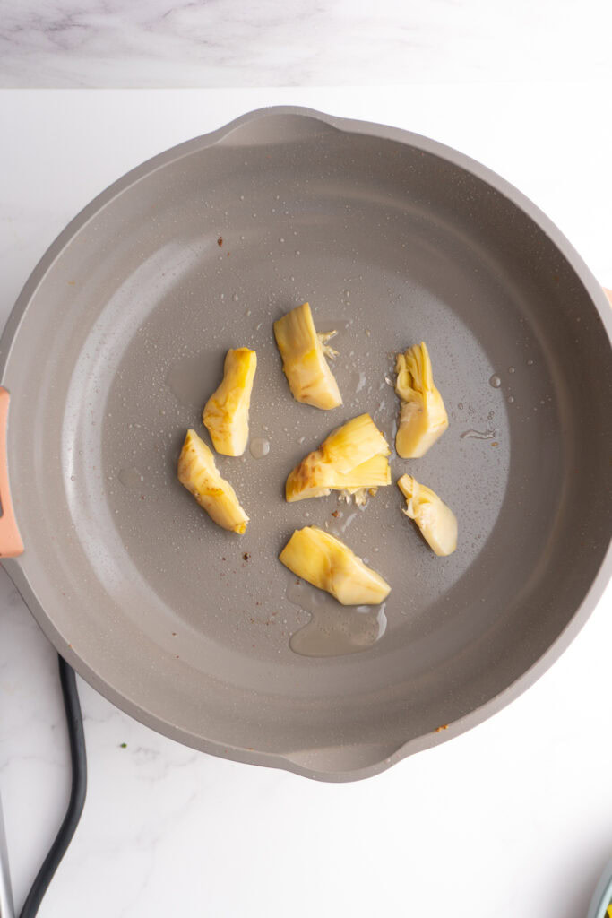 Quartered artichoke hearts searing in a skillet.