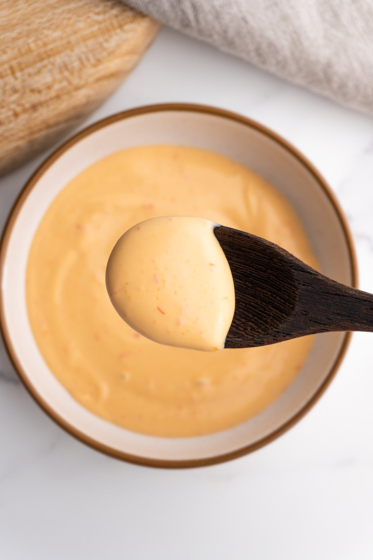 Overhead shot of a spoon with sriracha spicy mayo on it hovering over the bowl.