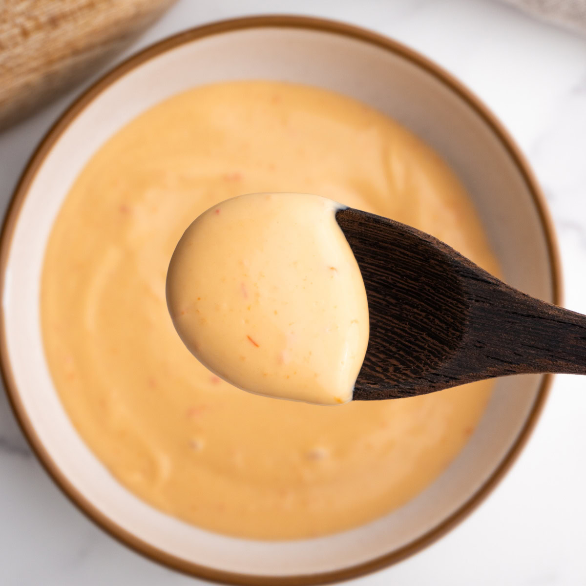 Spicy mayo on a spoon hovering over a bowl of it.