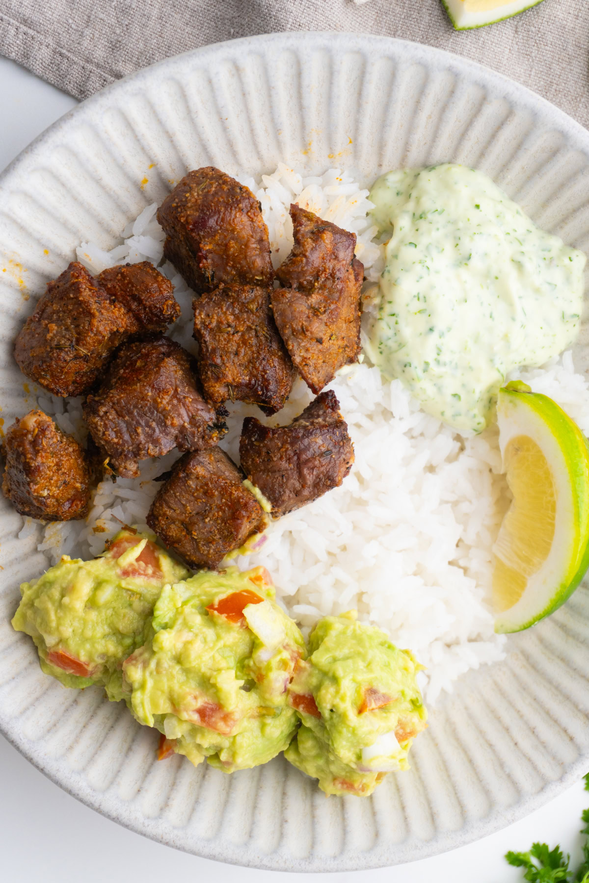 Steak taco bowls served with rice, guacamole, cilantro sauce and lime.