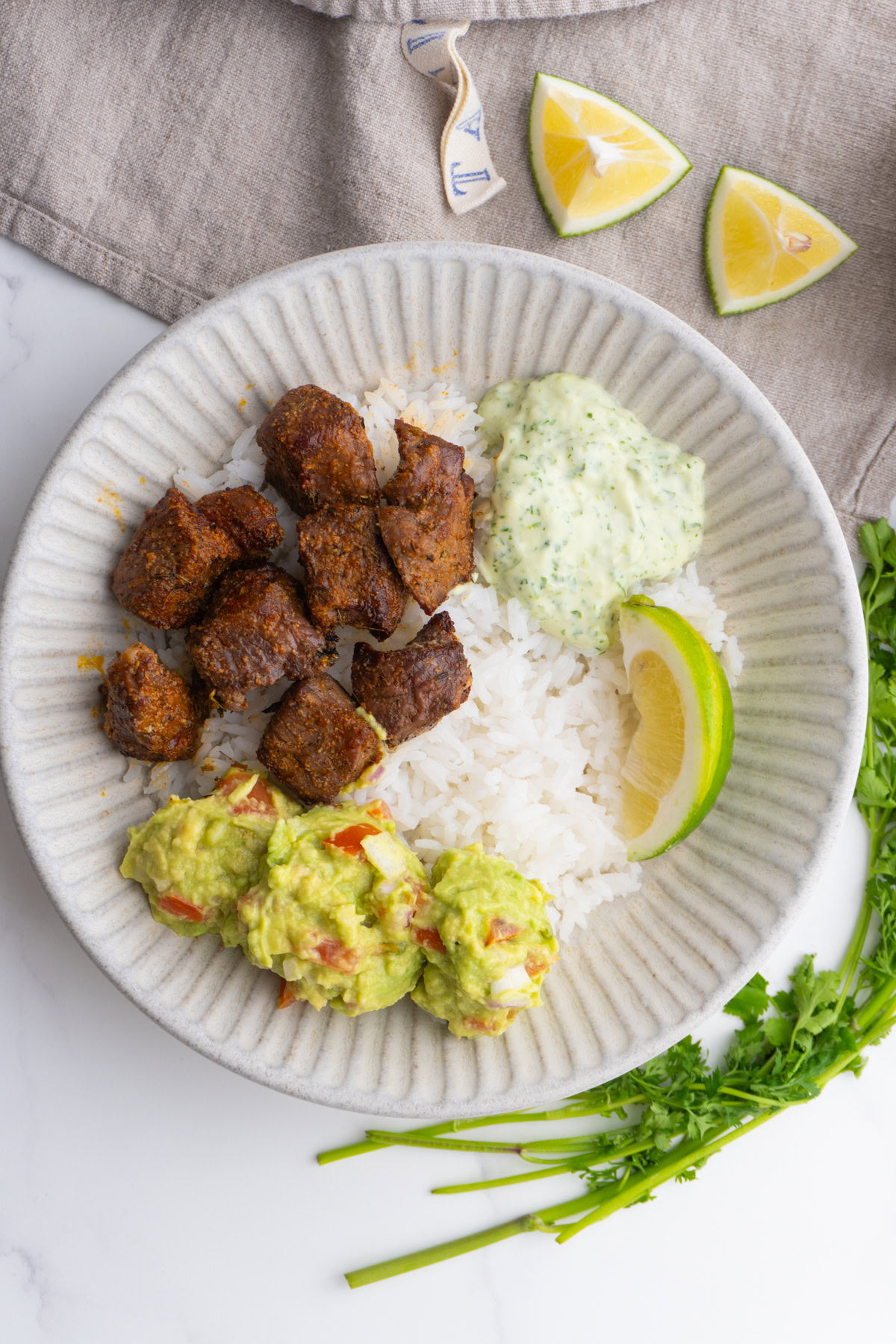 Steak bites, rice, sauce and guac in a bowl.