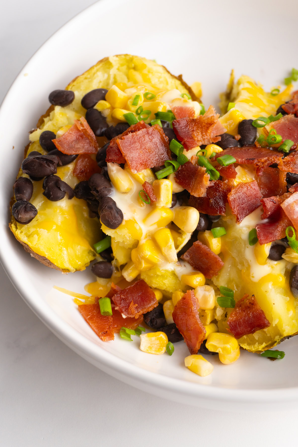 Side view of a loaded baked potato with bacon, corn, and green onions in a white bowl.