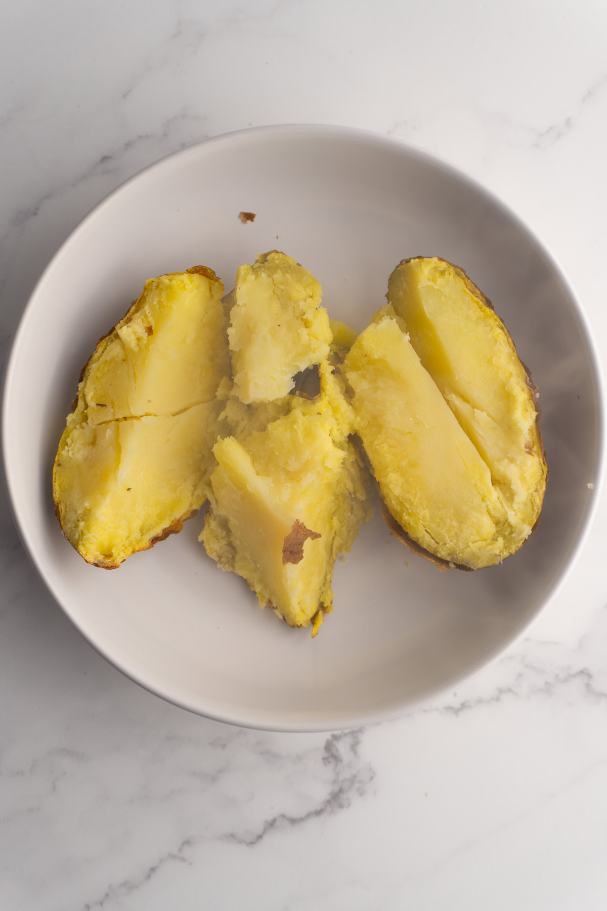 Baked potato broken open in a bowl.